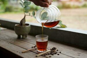 Holding a glass carafe, pour the black drip coffee into the cup and serve it in the morning. photo