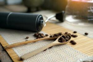 Roasted coffee beans in a wooden spoon and a coffee grinder on a woven bamboo placemat. It is a medium roast with medium intensity coffee flavor. photo