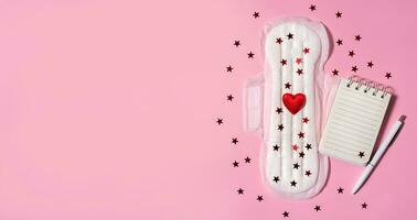 Sanitary napkin with red sequins and notepad on pink background. The period of the menstrual cycle. Notes. Banner. photo