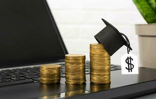 The concept of financial education. Gold coins with graduation hat stand on laptop on desktop photo