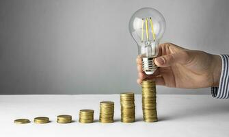 Business concept. A hand holds a lamp over coins on a light background. Business ideas, brainstorming. Recovery and business growth. Copy space photo