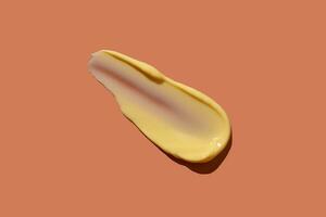 Yellow cosmetic smear of cream texture on a coral background. Skin care. Copy space. photo