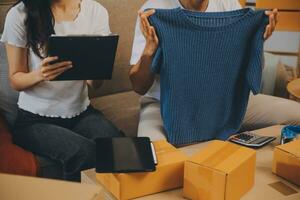 Two Asian blogger showing clothes in front of the camera to recording vlog video live streaming at her shop. Online Shopping Cart notion. on sofa at home photo