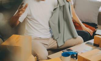 Two Asian blogger showing clothes in front of the camera to recording vlog video live streaming at her shop. Online Shopping Cart notion. on sofa at home photo