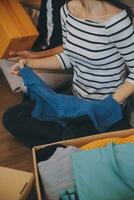 Two Asian blogger showing clothes in front of the camera to recording vlog video live streaming at her shop. Online Shopping Cart notion. on sofa at home photo