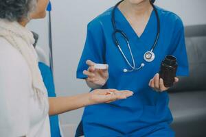 Asian woman nurse holding a medicine bottle and telling information to Asian senior woman before administering medication. Caregiver visit at home. Home health care and nursing home concept. photo