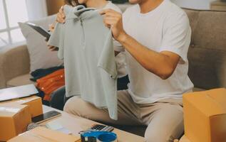 Two Asian blogger showing clothes in front of the camera to recording vlog video live streaming at her shop. Online Shopping Cart notion. on sofa at home photo