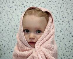 A little girl is wrapped in a towel after bathing. Close-up portrait. photo