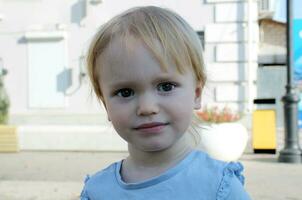 Portrait of a 2 year old blond girl on a background of leaves. Caucasian todler with big eyes looks at the camera and smiles. photo