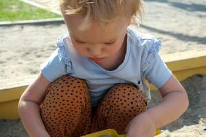 Little girl plays in the sandbox with toys. photo