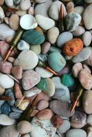 Parts of ammunition are visible from under the stones on the seashore vertical stock photo