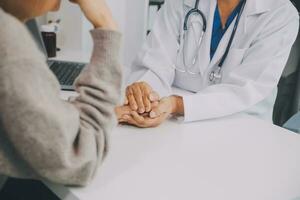 Doctor and patient sitting near each other at the table in clinic office. The focus is on female physician's hands reassuring woman, only hands, close up. Medicine concept photo