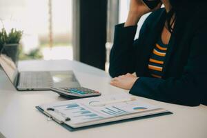 Charming Young asian businesswoman sitting on laptop computer in the office, making report calculating balance Internal Revenue Service checking document. photo