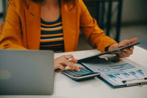 encantadora joven mujer de negocios asiática sentada en una computadora portátil en la oficina, haciendo un informe que calcula el documento de verificación del servicio de ingresos internos del saldo. foto