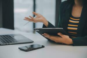 encantadora joven mujer de negocios asiática sentada en una computadora portátil en la oficina, haciendo un informe que calcula el documento de verificación del servicio de ingresos internos del saldo. foto