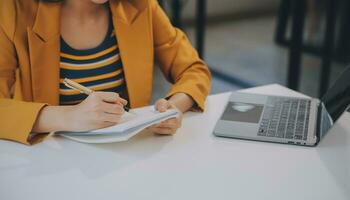 encantadora joven mujer de negocios asiática sentada en una computadora portátil en la oficina, haciendo un informe que calcula el documento de verificación del servicio de ingresos internos del saldo. foto