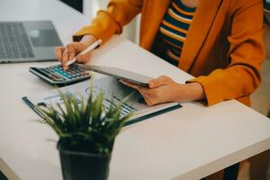 Charming Young asian businesswoman sitting on laptop computer in the office, making report calculating balance Internal Revenue Service checking document. photo