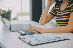 Charming Young asian businesswoman sitting on laptop computer in the office, making report calculating balance Internal Revenue Service checking document. photo