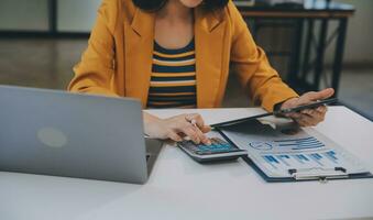 encantadora joven mujer de negocios asiática sentada en una computadora portátil en la oficina, haciendo un informe que calcula el documento de verificación del servicio de ingresos internos del saldo. foto