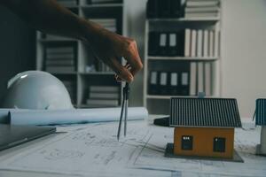 architectural model of houses on desk with drawing technical tools and blueprint rolls, isolated on white background, for building construction plan, interior designer and architect work concept photo