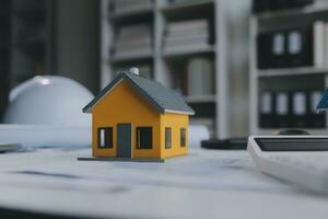 architectural model of houses on desk with drawing technical tools and blueprint rolls, isolated on white background, for building construction plan, interior designer and architect work concept photo