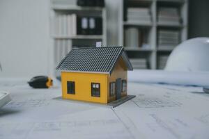 architectural model of houses on desk with drawing technical tools and blueprint rolls, isolated on white background, for building construction plan, interior designer and architect work concept photo