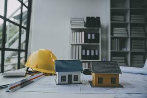 architectural model of houses on desk with drawing technical tools and blueprint rolls, isolated on white background, for building construction plan, interior designer and architect work concept photo