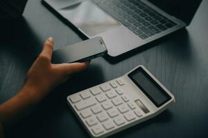 Asian Business woman using calculator and laptop for doing math finance on an office desk, tax, report, accounting, statistics, and analytical research concept photo