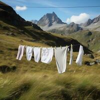 AI Generated After washing, white clean laundry dries on a rope in a field against the backdrop of the Alpine mountains photo