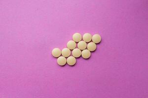 Yellow pills isolated on a pink background. Top view, flat lay. photo