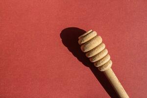 Wooden honey dipper isolated on a red background. Copy space for text. photo