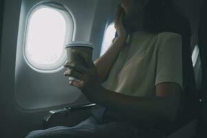 Asian woman enjoying enjoys a coffee comfortable flight while sitting in the airplane cabin, Passengers near the window. photo