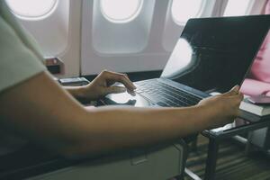 Asian woman passenger sitting in airplane near window and reading news from social networks or using travel applications in smartphone photo