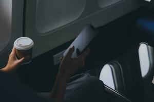 Asian woman enjoying enjoys a coffee comfortable flight while sitting in the airplane cabin, Passengers near the window. photo