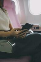 Asian woman passenger sitting in airplane near window and reading news from social networks or using travel applications in smartphone photo