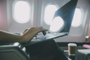 Asian woman passenger sitting in airplane near window and reading news from social networks or using travel applications in smartphone photo