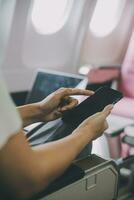 Asian woman passenger sitting in airplane near window and reading news from social networks or using travel applications in smartphone photo