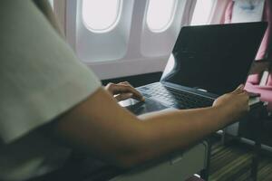 Asian woman passenger sitting in airplane near window and reading news from social networks or using travel applications in smartphone photo