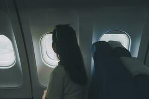 Silhouette of woman looks out the window of an flying airplane. Passenger on the plane resting beside the window. photo