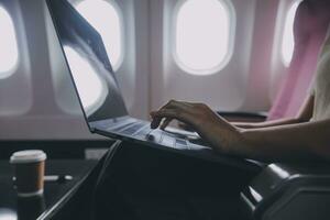 Asian woman passenger sitting in airplane near window and reading news from social networks or using travel applications in smartphone photo