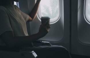 Asian woman enjoying enjoys a coffee comfortable flight while sitting in the airplane cabin, Passengers near the window. photo