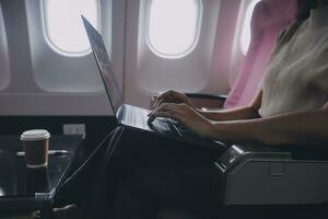 Asian woman passenger sitting in airplane near window and reading news from social networks or using travel applications in smartphone photo