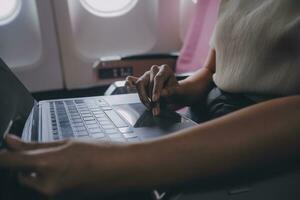 Asian woman passenger sitting in airplane near window and reading news from social networks or using travel applications in smartphone photo
