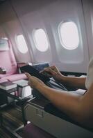Asian woman passenger sitting in airplane near window and reading news from social networks or using travel applications in smartphone photo