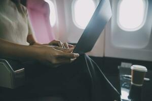 Asian woman passenger sitting in airplane near window and reading news from social networks or using travel applications in smartphone photo