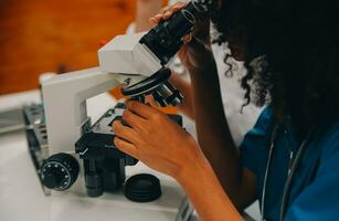 médico trabajador en laboratorio Saco y estéril mascarilla, haciendo un microscopio análisis mientras su colega son trabajando detrás foto