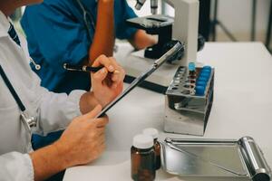 Medical worker in lab coat and sterile mask, doing a microscope analysis while her colleague are working behind photo