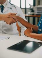 Doctor and patient shaking hands in the office, they are sitting at desk, hands close up photo