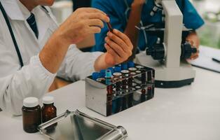 médico trabajador en laboratorio Saco y estéril mascarilla, haciendo un microscopio análisis mientras su colega son trabajando detrás foto