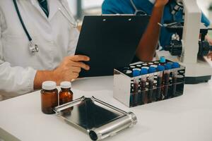 Medical worker in lab coat and sterile mask, doing a microscope analysis while her colleague are working behind photo